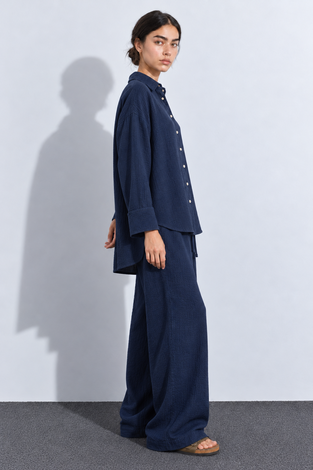 Side view of a navy crinkle co-ord set showing the relaxed shirt, broad sleeve cuffs and roomy trousers.